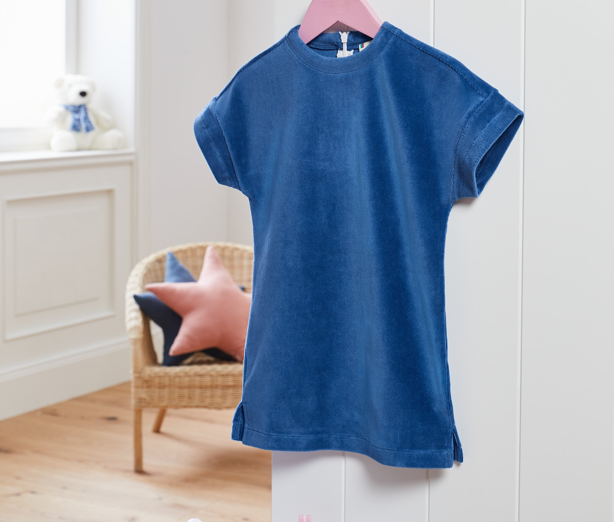 Ein blaues Stretch-Cordkleid hängt an einem pinkfarbenen Bügel.