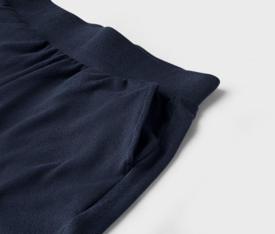 Detailaufnahme einer dunkelblauen Jogginghose mit Tasche auf weißem Hintergrund.