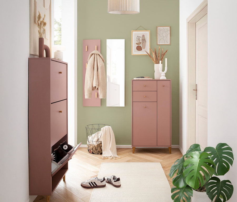 Flur mit rosa Schuhschrank, Garderobe, Spiegel und Kommode vor einer grünen Wand.