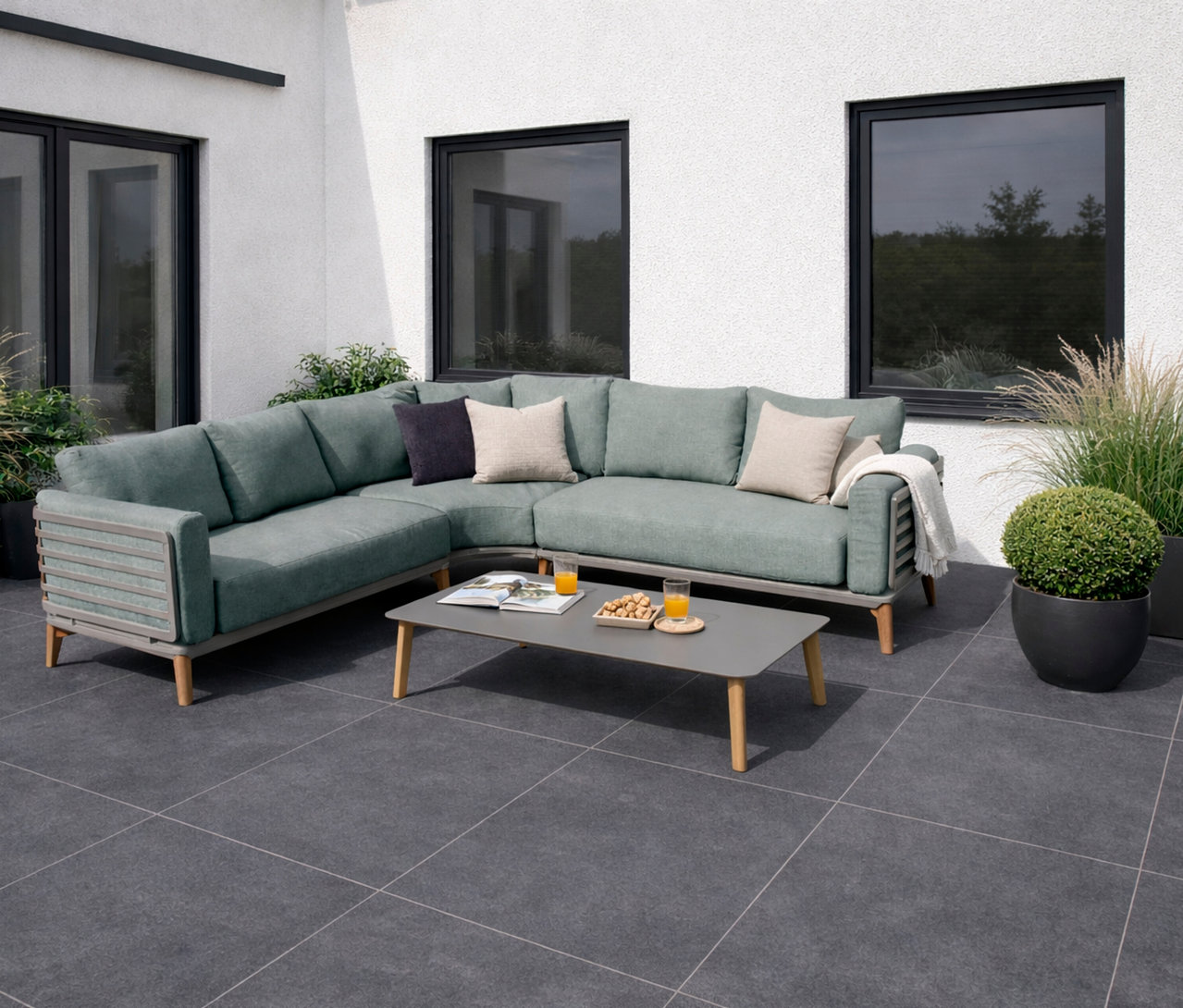 Salbeigrüne Leco Lounge-Ecke »Moss« mit Tisch auf einer Terrasse vor einem weißen Haus mit Fenstern und Pflanzen.