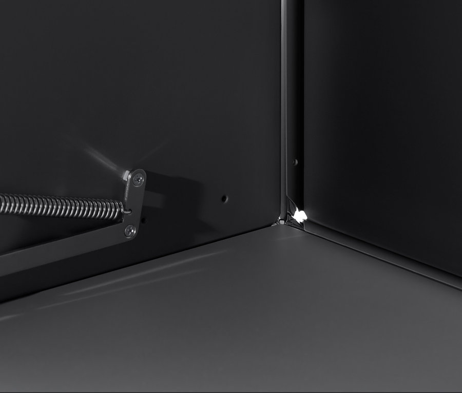 Detailansicht des Innenraums eines schwarzen »CN3« Schranks mit Klappe, Fokus auf Ecke und Öffnungsmechanismus.