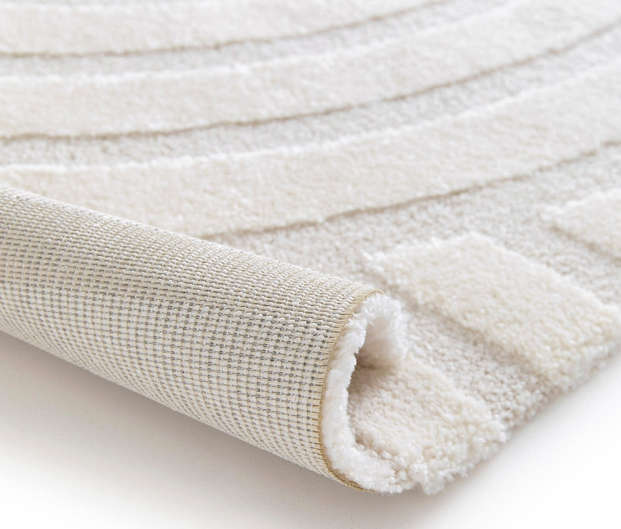 Detailansicht eines beigen Teppichs »Cosmo«, der aufgerollt auf einem weißen Hintergrund liegt.