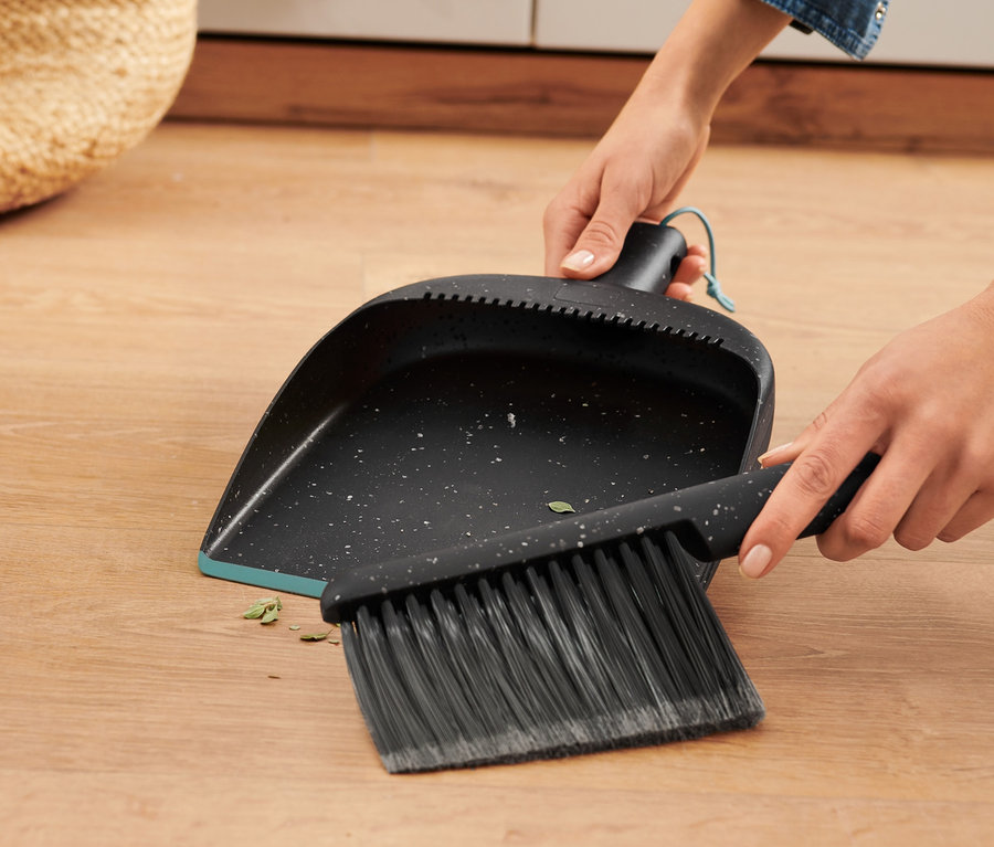 Frau kehrt mit Handkehrer und Schaufel Schmutz vom Holzboden.