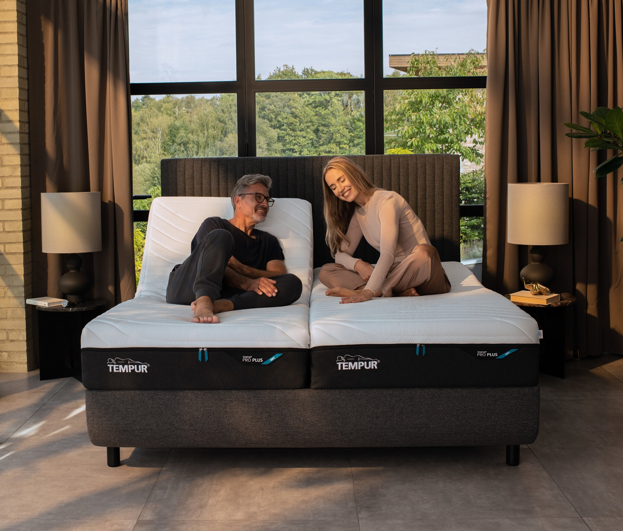 Mann und Frau sitzen auf einem Bett mit TEMPUR® Systemrahmen elektrisch verstellbarer Lattenrost »Premium Flex 3000«.
