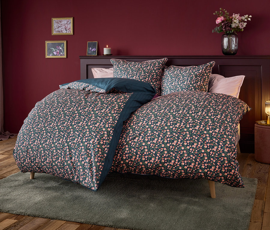 Bett mit marineblauer Bettwäsche mit Blumenmuster.