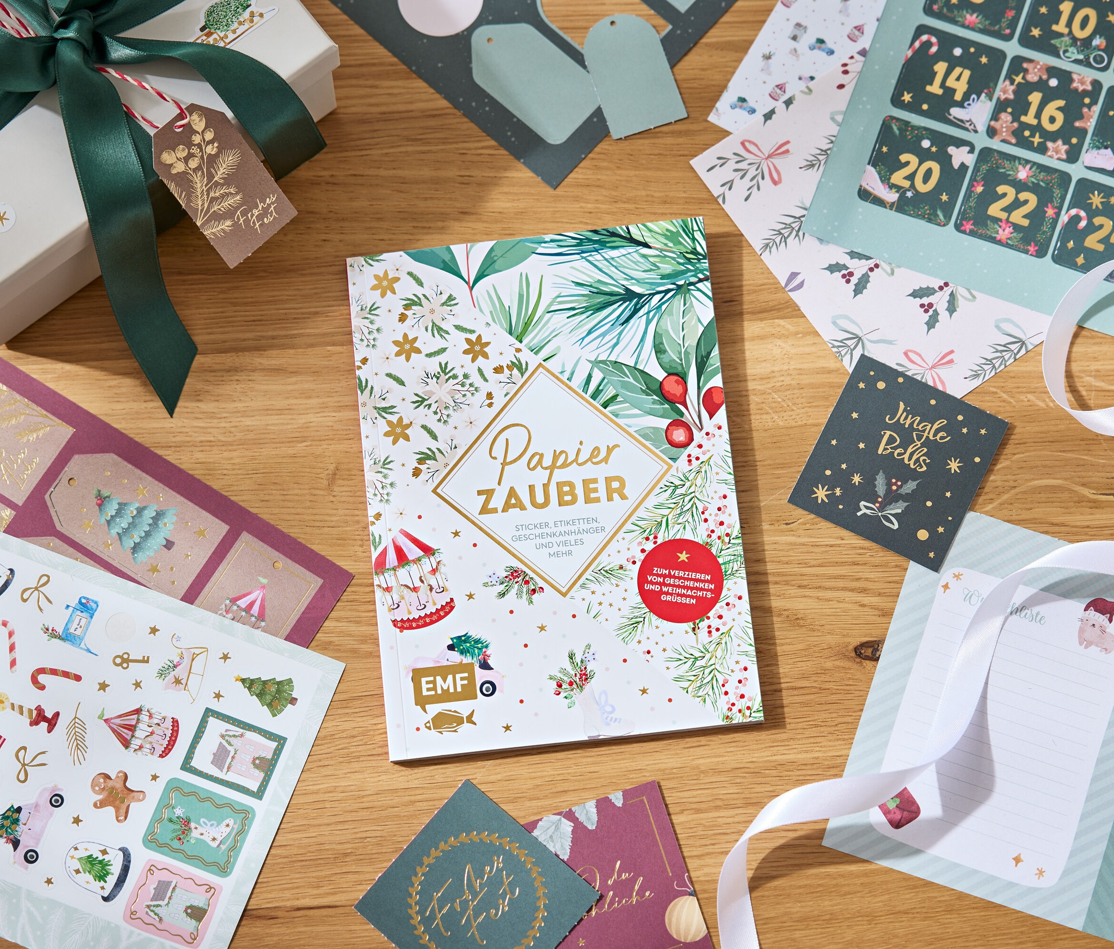 Dekorative Papiere, Aufkleber und eine Geschenkbox mit Schleife auf einem Holztisch.