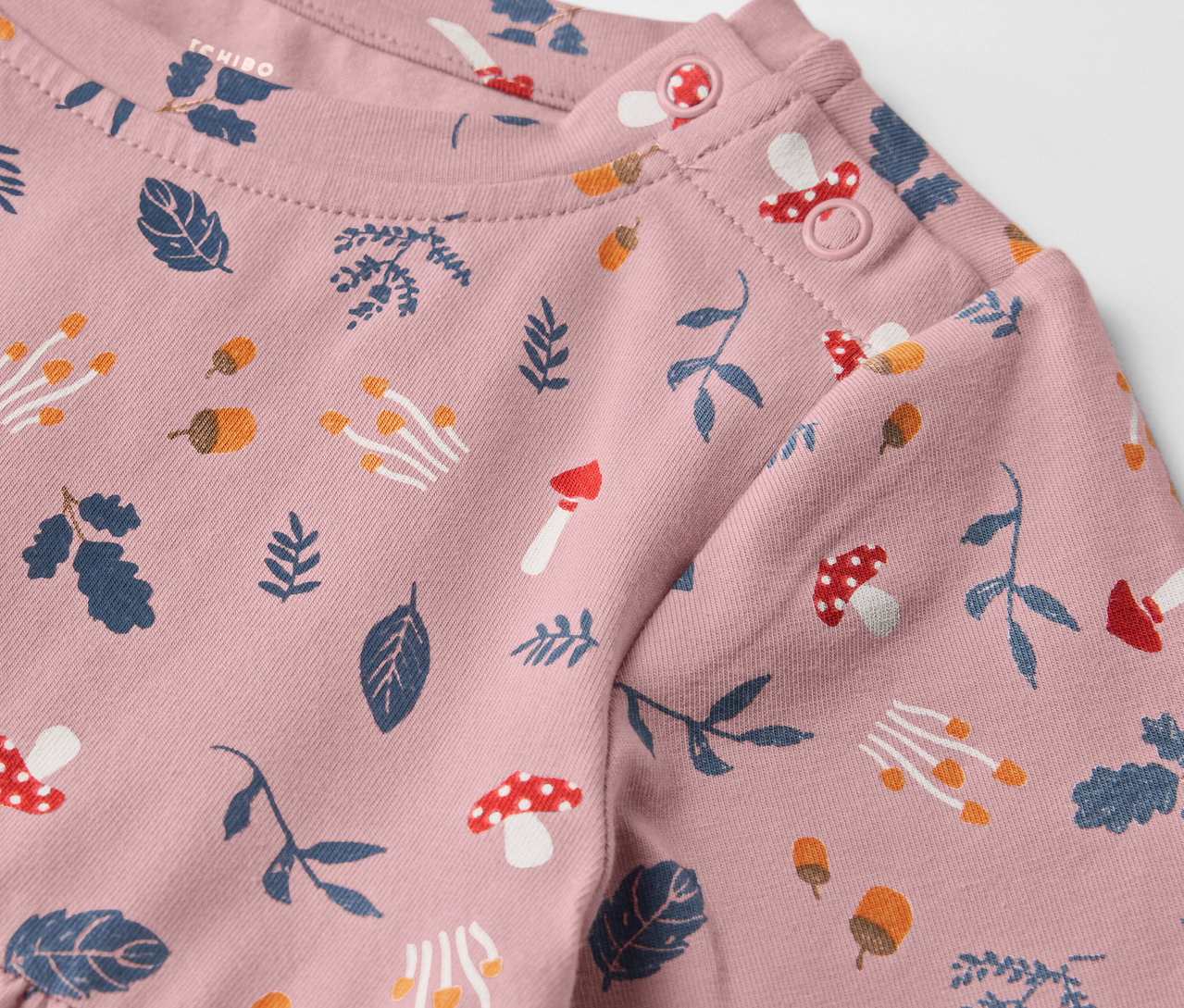Detailansicht eines rosa Kinder-Jerseykleids mit Blätter- und Pilzaufdruck.