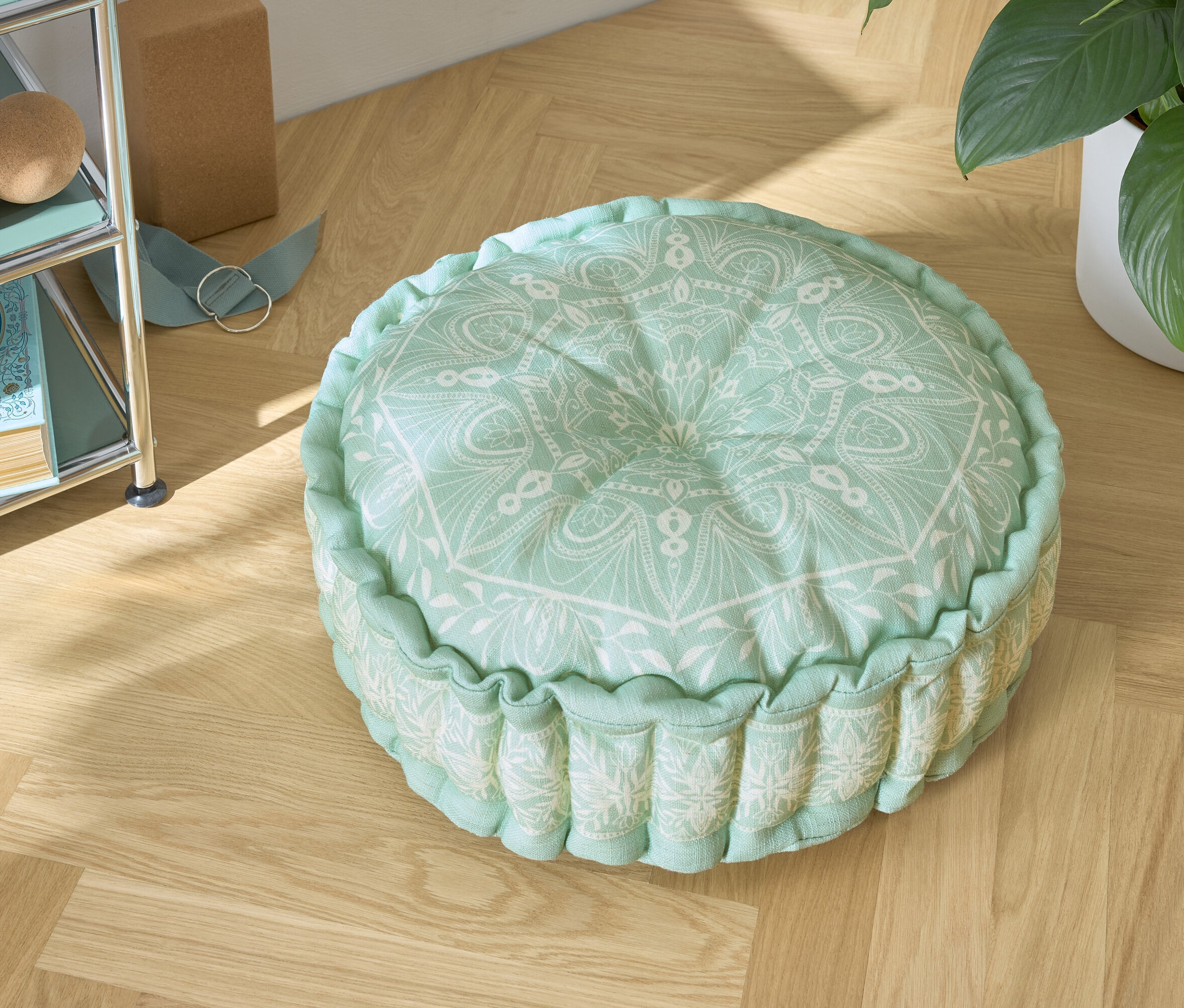 Ein grünes Sitzkissen mit weißem Muster auf einem Holzboden.