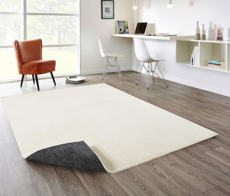 Ein wollweißer Teppich »Mellow« liegt auf einem Holzboden in einem Wohnzimmer.