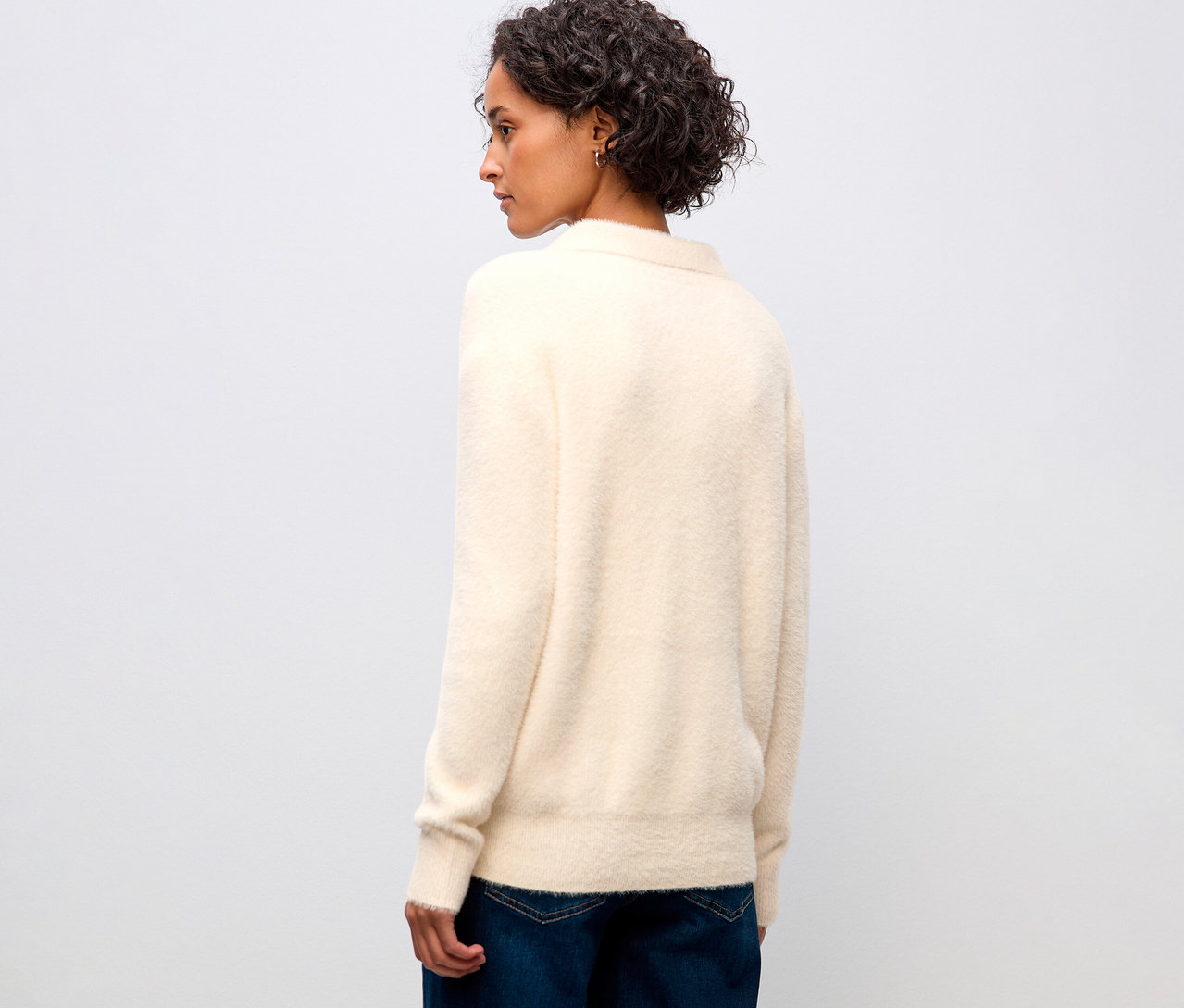 Frau von hinten, mit beigem Street One Strickpullover mit Polokragen und Jeans.
