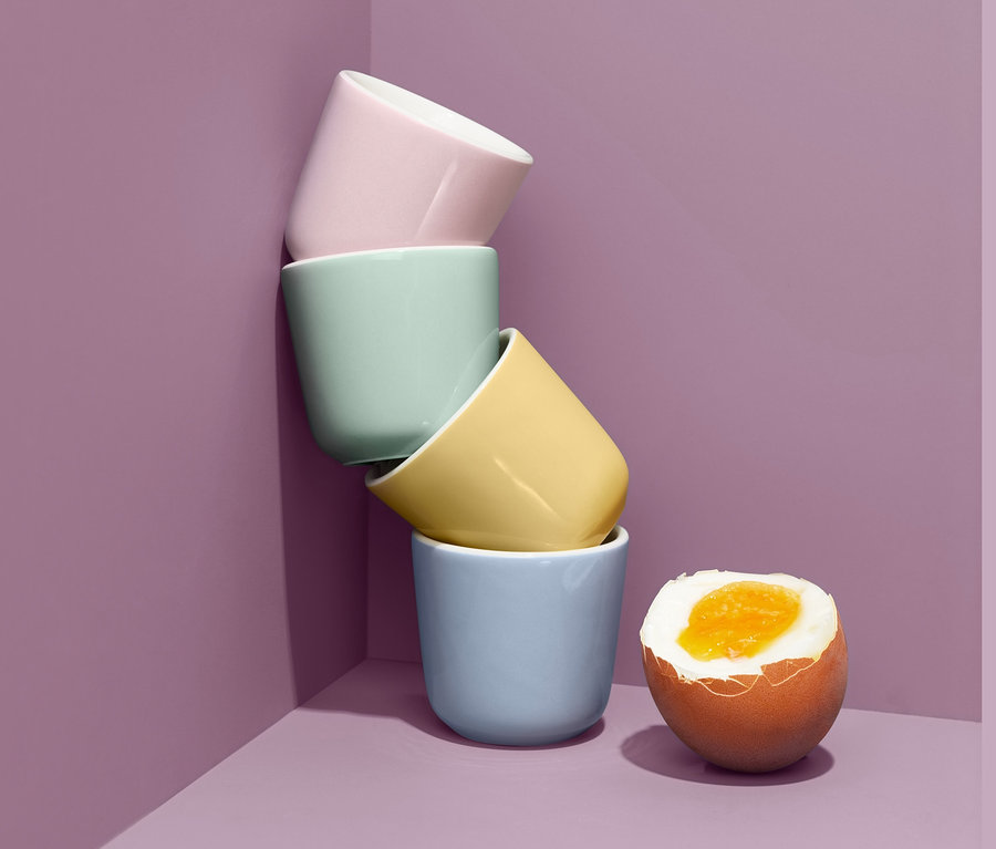 Vier pastellfarbene Eierbecher sind neben einem gekochten Ei aufeinander gestapelt.