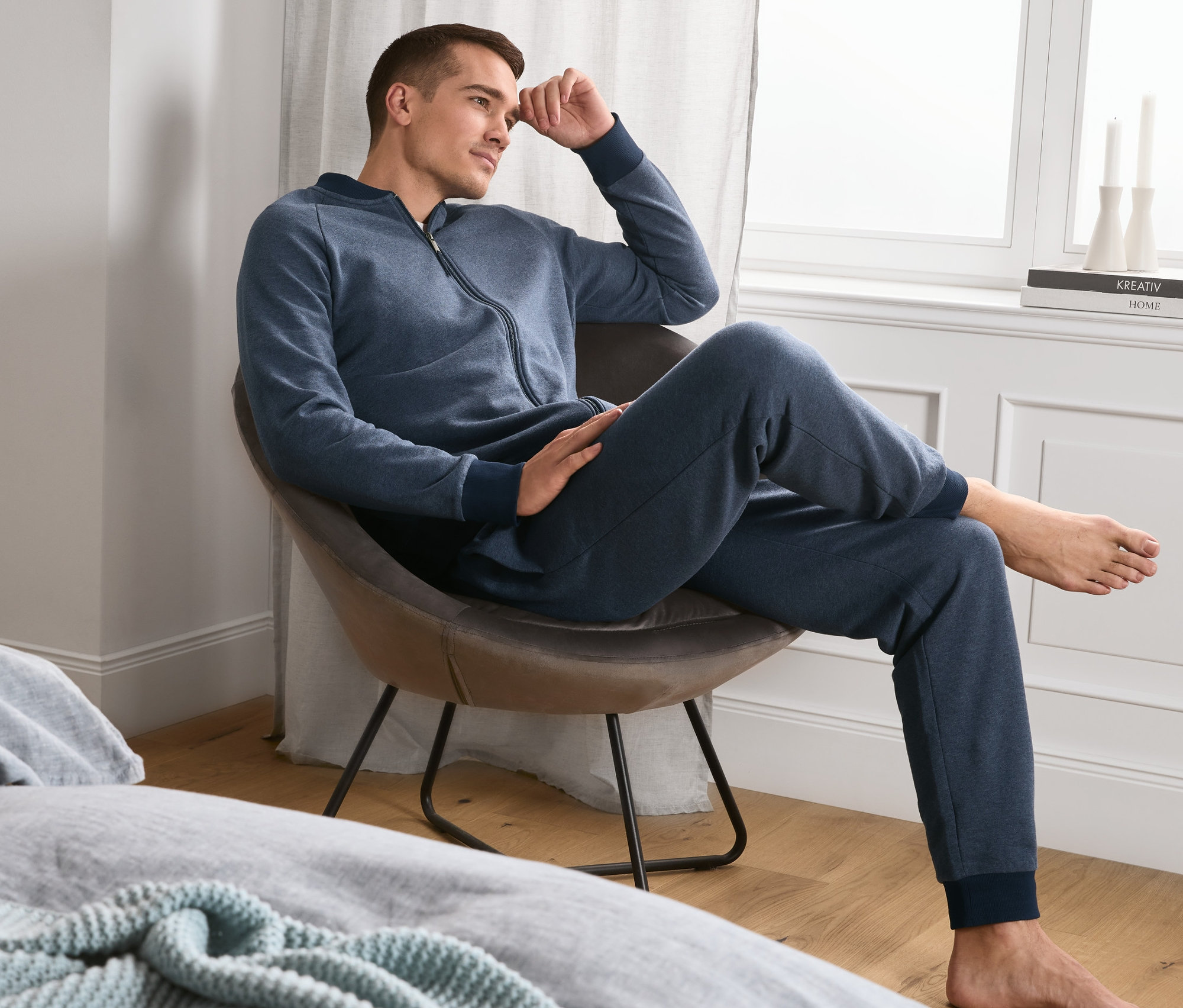 Mann sitzt in einem Sessel und trägt einen blauen Hausanzug in weicher Sweatqualität.