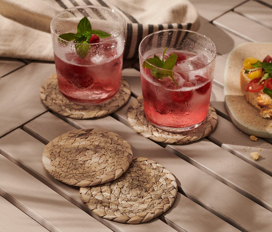 Zwei Getränke mit Eis auf 4 Untersetzern für Gläser, neben einem Teller mit belegten Broten.