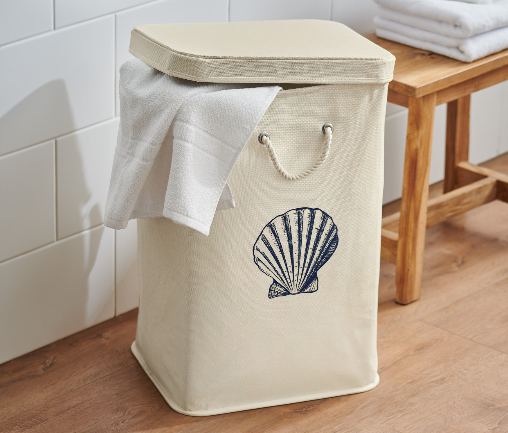 Ein cremefarbener Wäschesammler mit Deckel und Muscheldruck steht im Badezimmer.