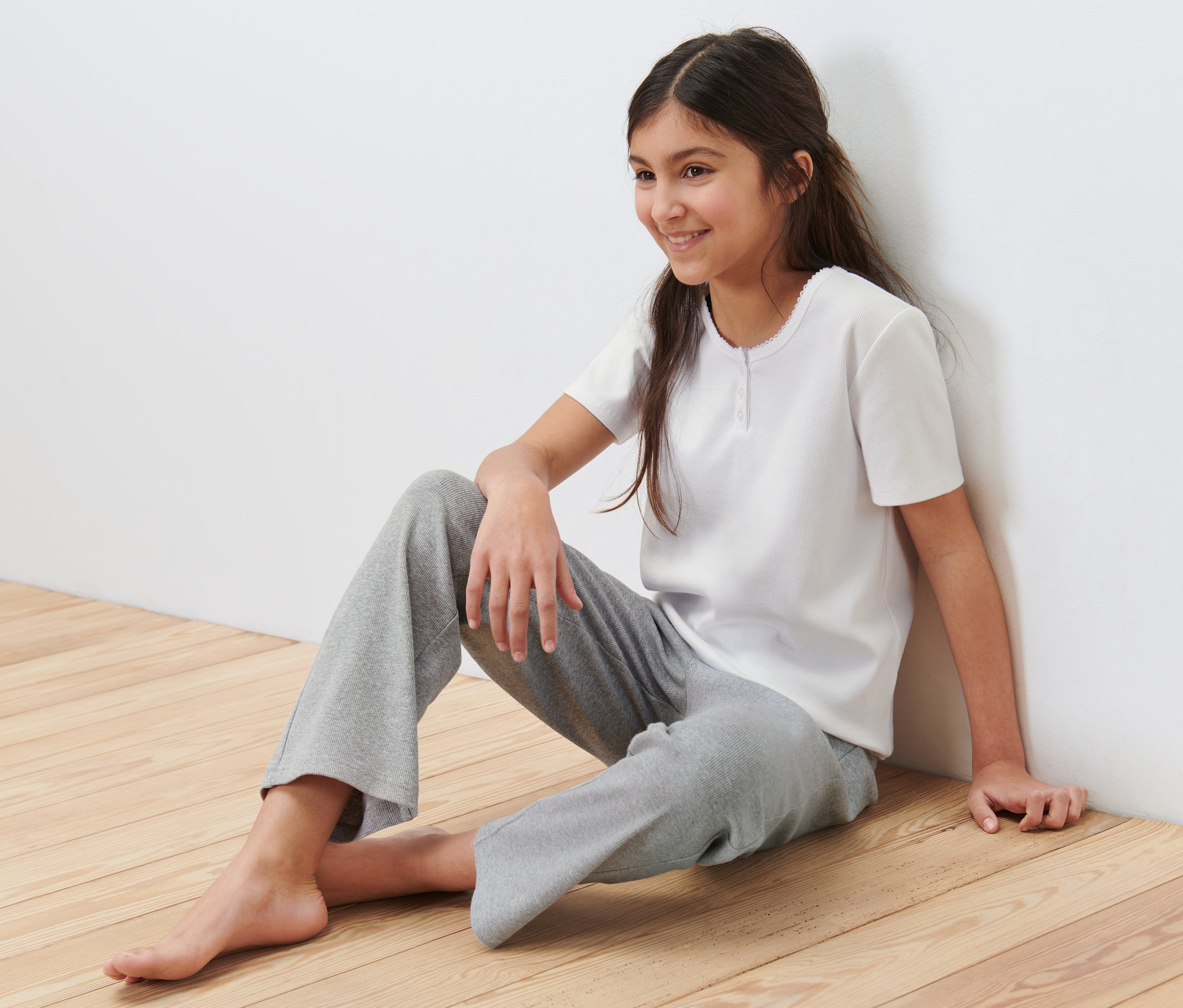 Ein Mädchen sitzt auf dem Boden und trägt einen Kinder-Ripp-Pyjama.