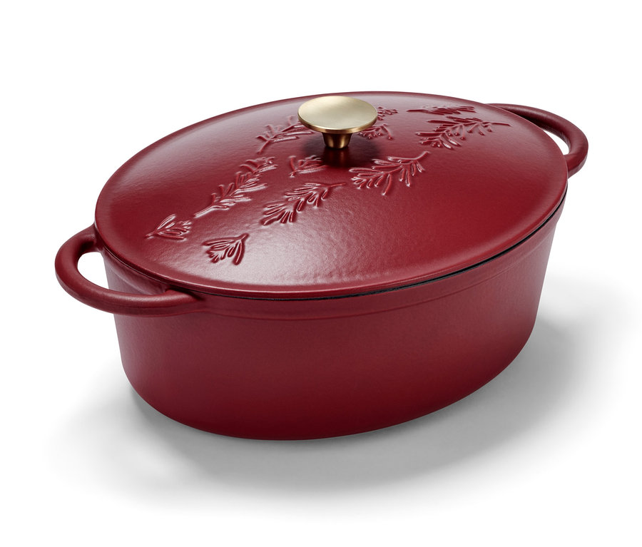 Ein roter, ovaler Gusseisenbräter mit einem Deckel, der mit einem Blattmotiv verziert ist.