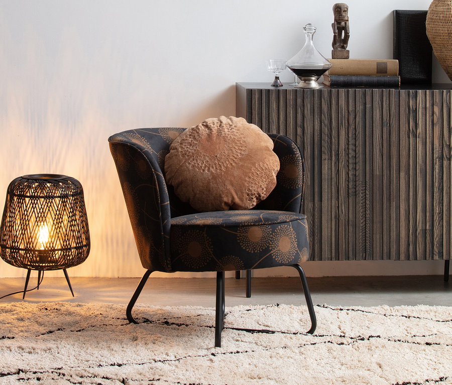 Schwarze Lampe steht auf beigem Woood Teppich Cleo neben Sessel mit braunem Kissen.