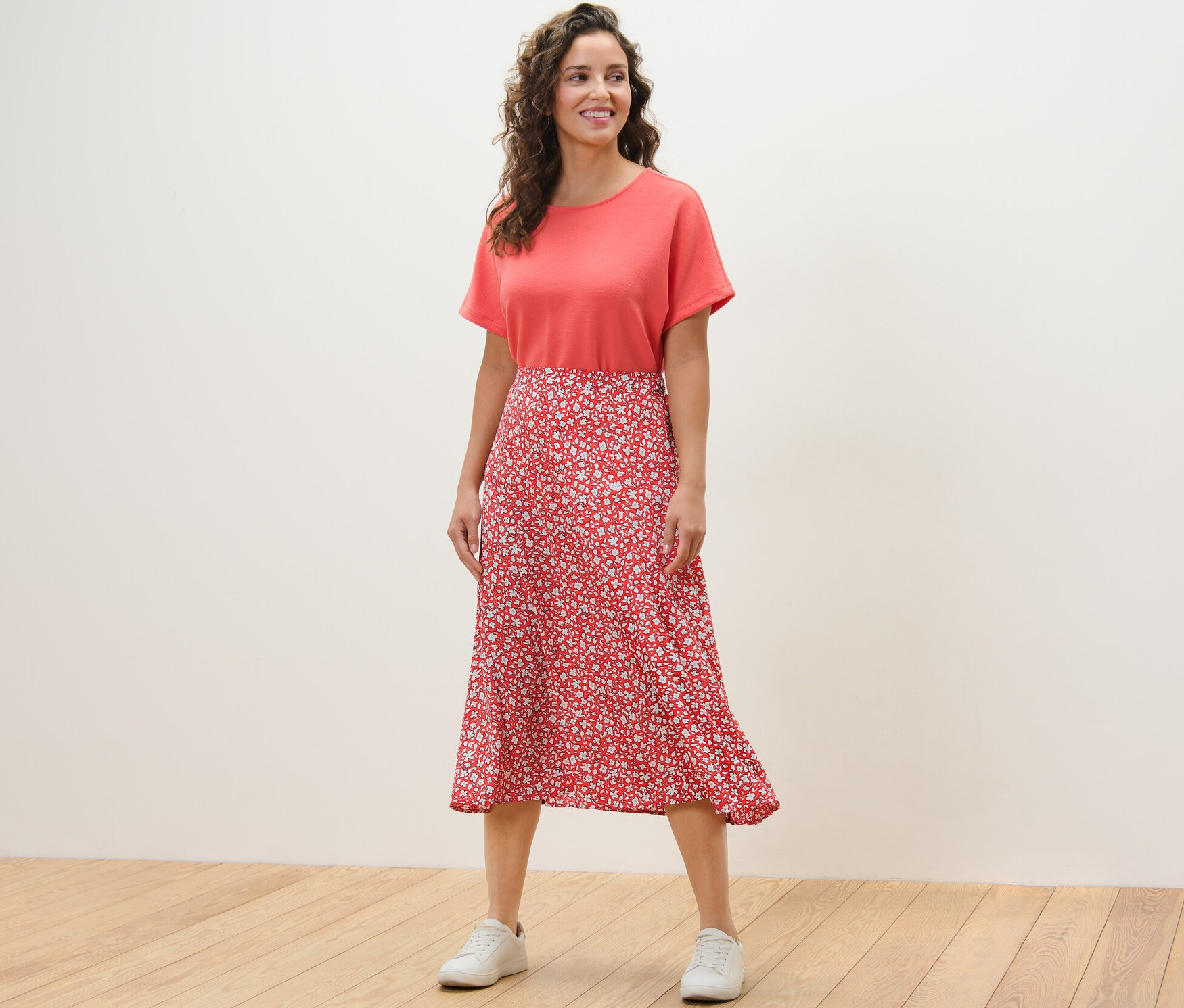 Eine Frau steht auf einem Holzboden und trägt einen korallfarbenen, bedruckten Midirock.