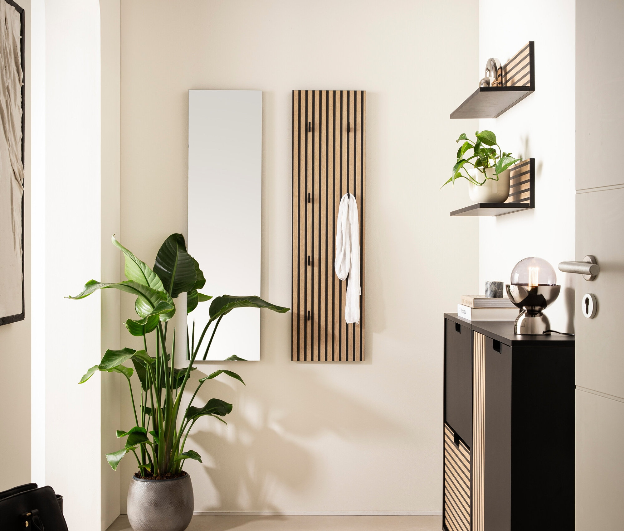 Eingangsbereich mit Spiegel, Garderobe, Schuhschrank, zwei Regalen, Pflanze und runder Beleuchtung.