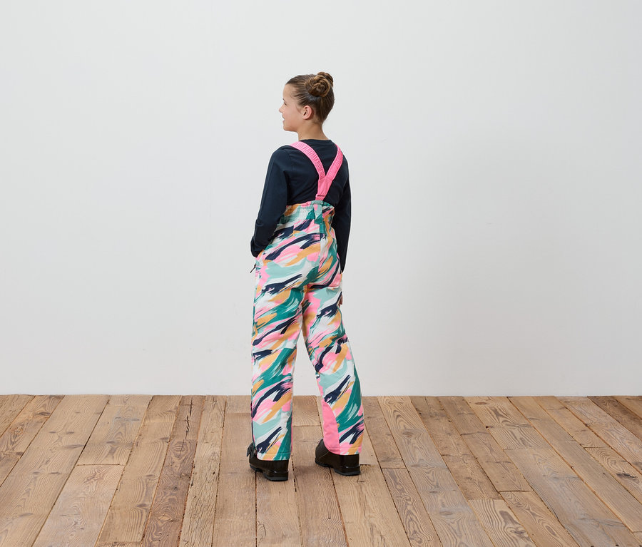 Ein Mädchen in einer Latzhose mit buntem Muster steht mit dem Rücken zur Kamera.