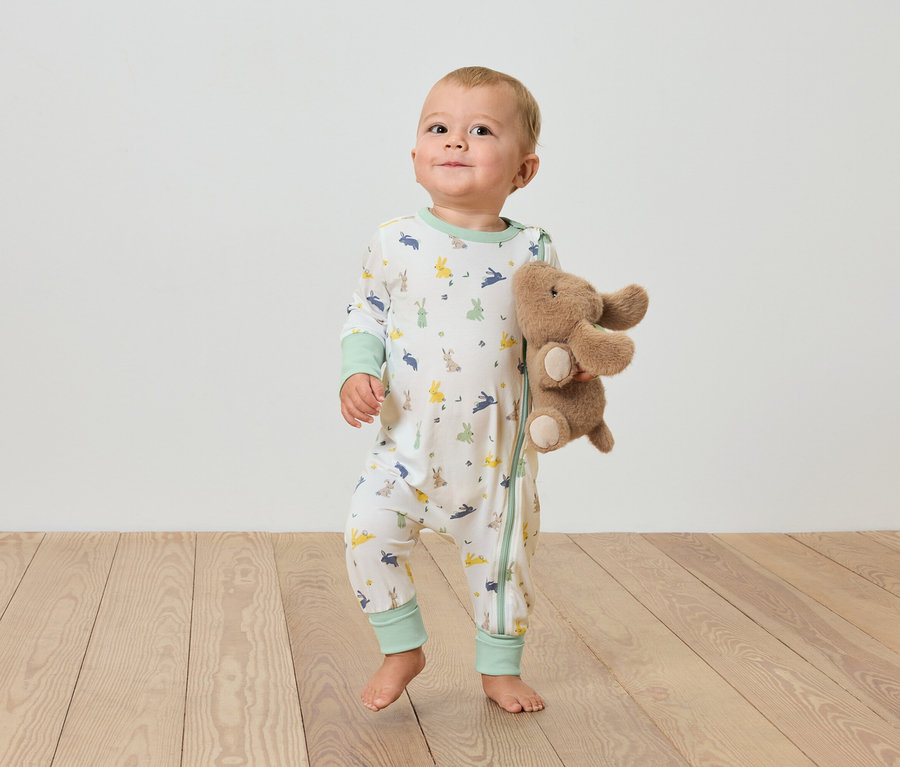 Ein Baby steht auf einem Holzboden und hält einen Plüsch-Elefanten.