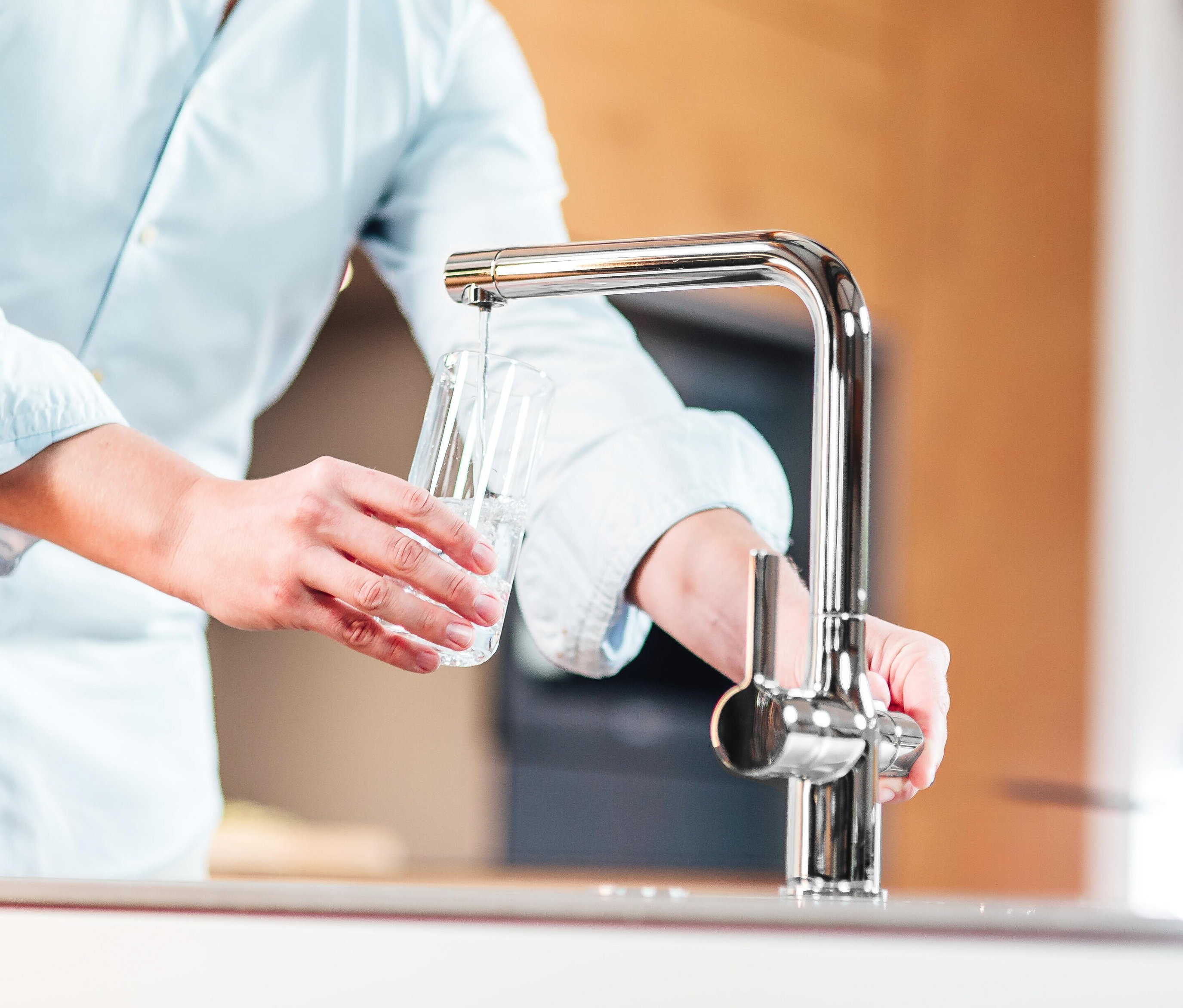Mann füllt Wasser aus einer verchromten Schütte AQUASTAR PRO Filterarmatur in ein Glas.