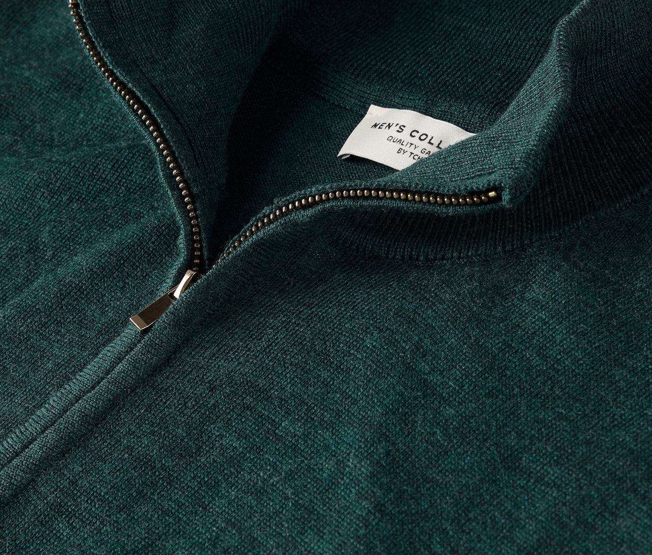 Detailansicht eines grünen Pullovers mit Reißverschluss und Etikett.