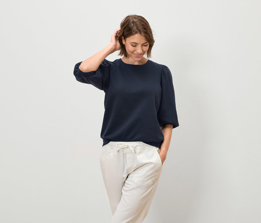 Frau posiert in marineblauer Bluse mit kurzen Ärmeln und heller Hose.