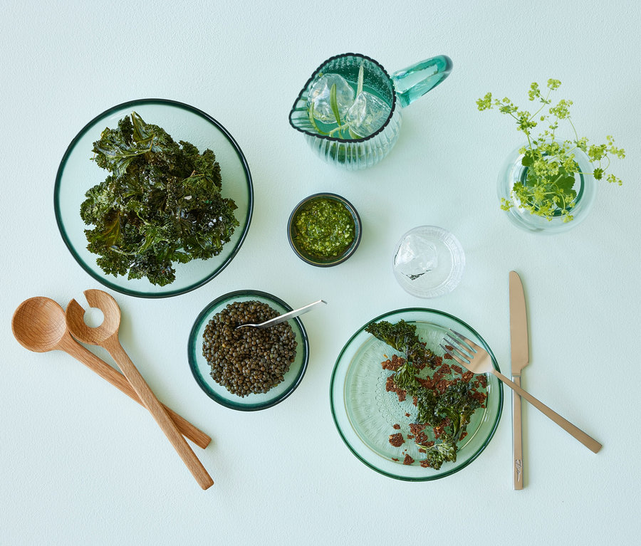 Grüne Bitz Glasteller »Kusintha« mit Grünkohlchips, Kaviar und Dip auf einem Tisch.