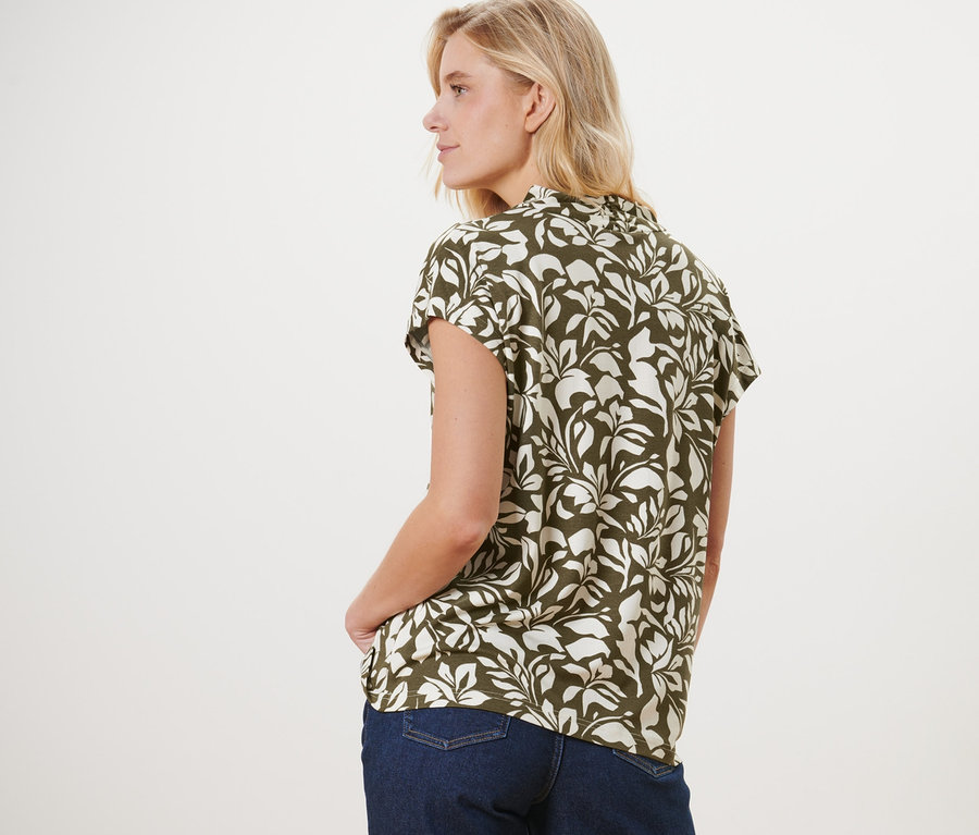 Frau steht mit dem Rücken zur Kamera und trägt ein bedrucktes Blusenshirt mit V-Ausschnitt und Jeans.