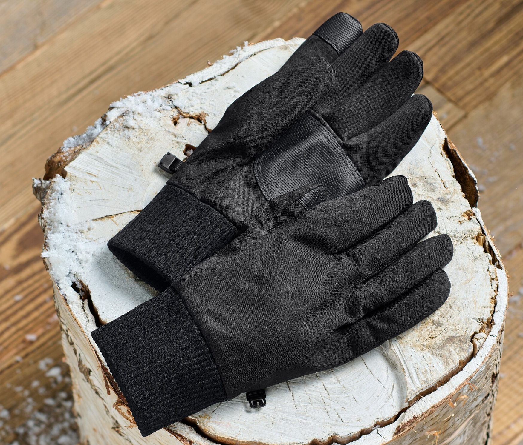 Schwarze Softshell-Handschuhe liegen auf einem Holzscheit.