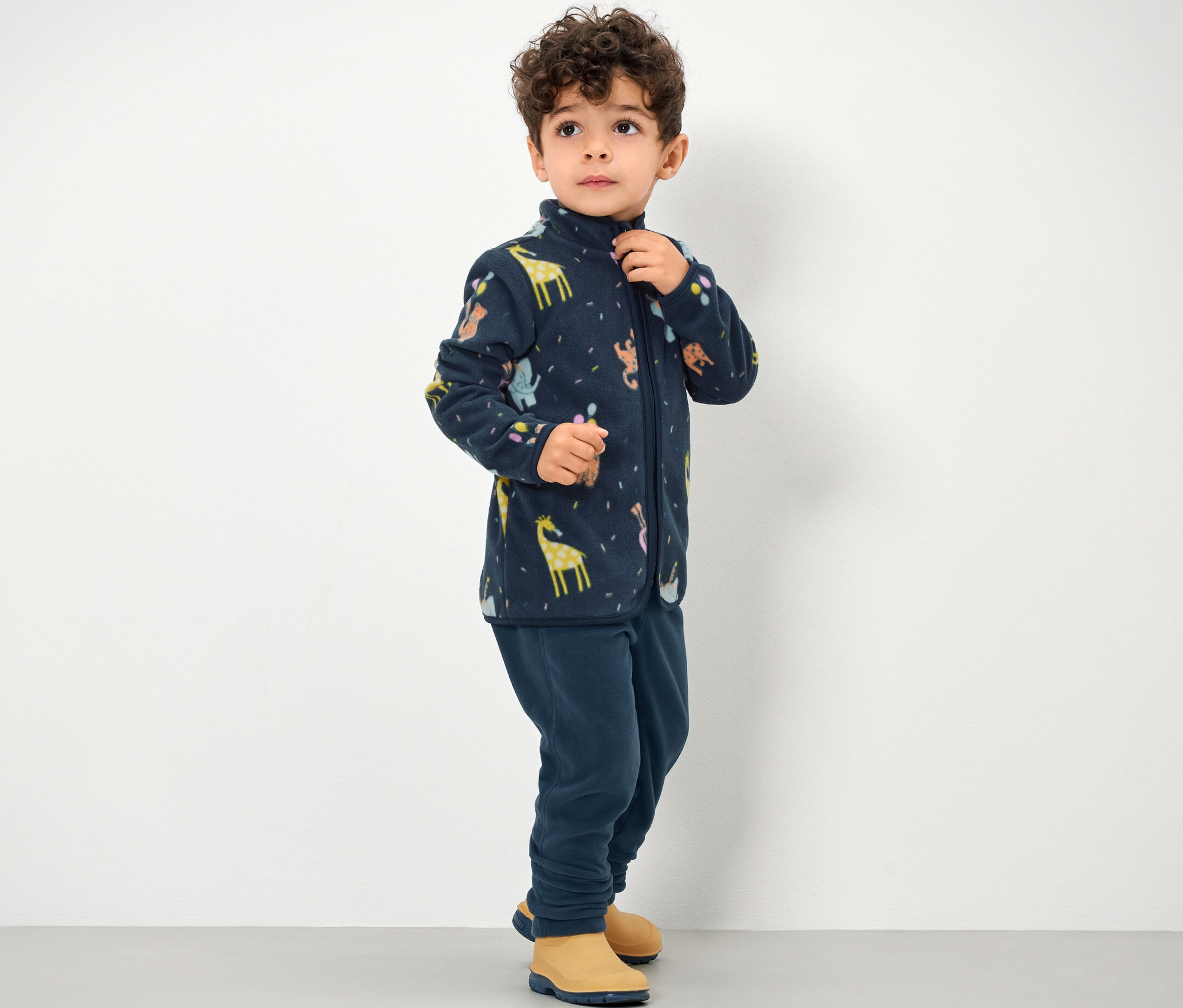 Ein Junge trägt eine Kinder-Fleecehose und eine Reissverschlussjacke mit Tiermuster.