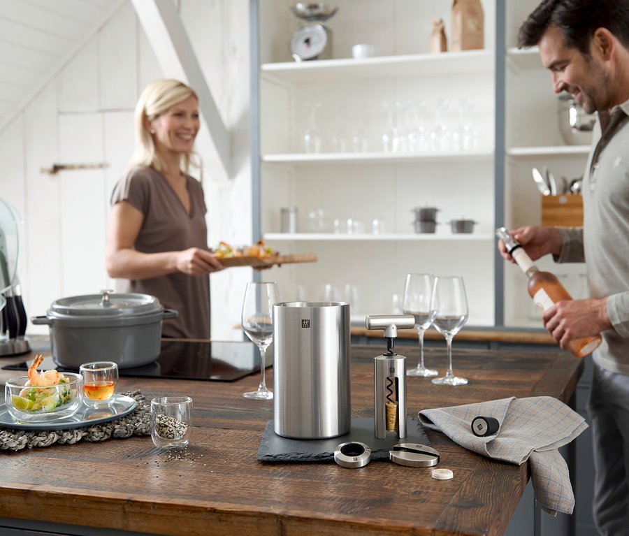 Mann öffnet Weinflasche mit ZWILLING Sommelier-Set, 4-teilig, während Frau Tablett mit Essen trägt.