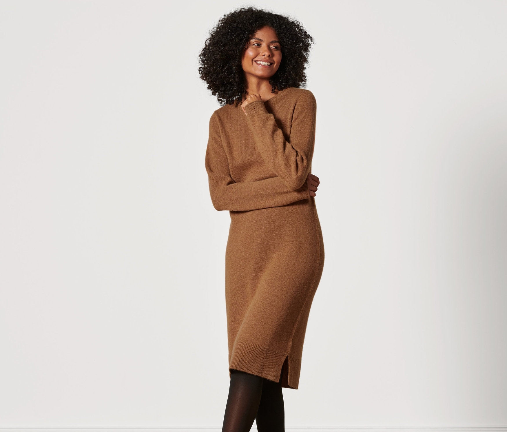 Frau mit dunklen lockigen Haaren posiert in braunem Premium Woll-Cashmere-Strickkleid.