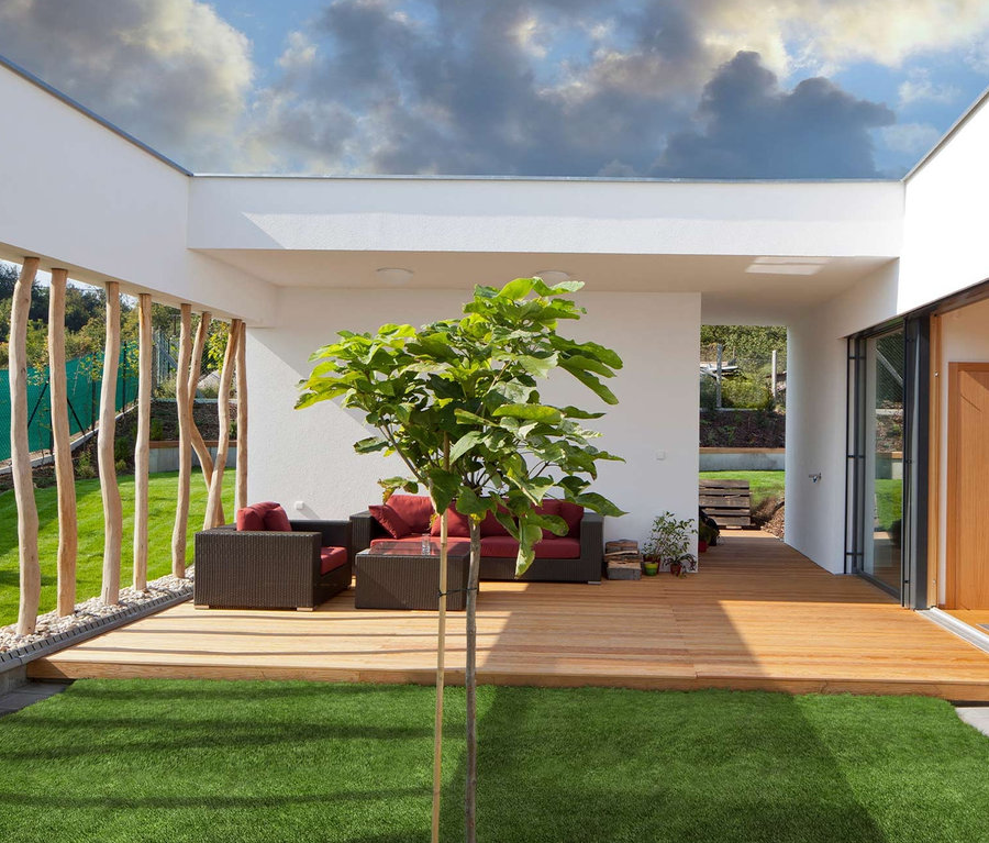 Außenterrasse mit braunen Sitzen mit roten Kissen, Holzboden und grünem Primaflor Kunstrasen.