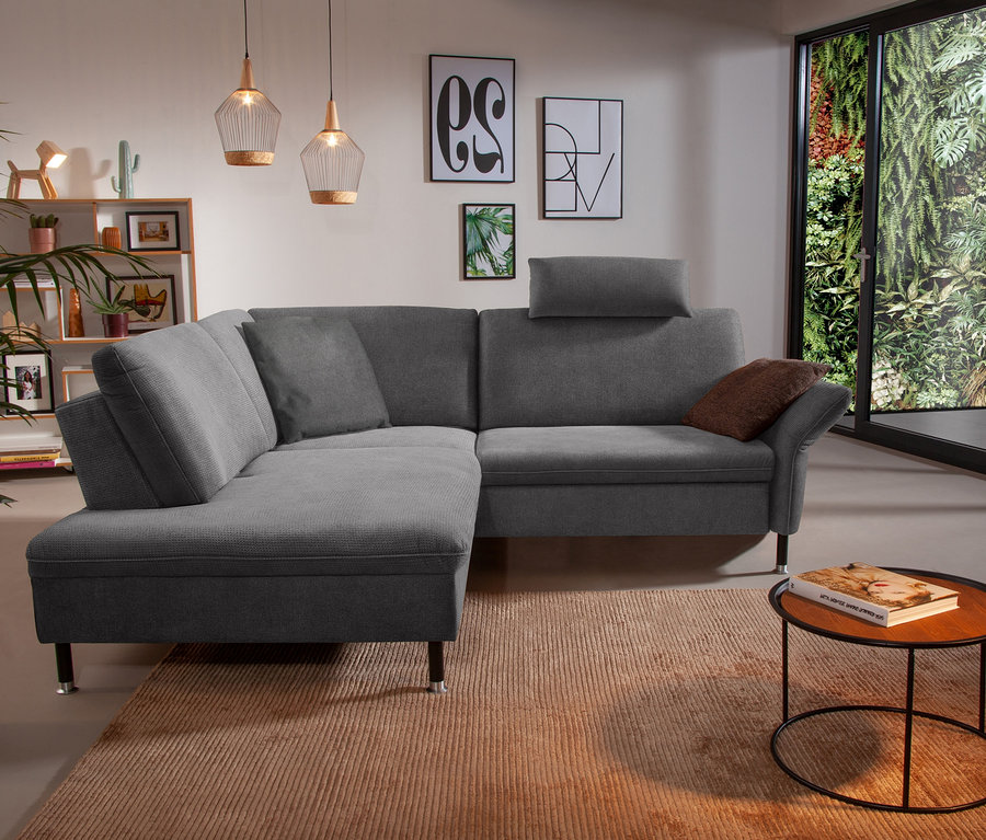 Wohnzimmer mit linksseitigem Ecksofa "Jonas" in Quarzgrau auf einem Teppich.