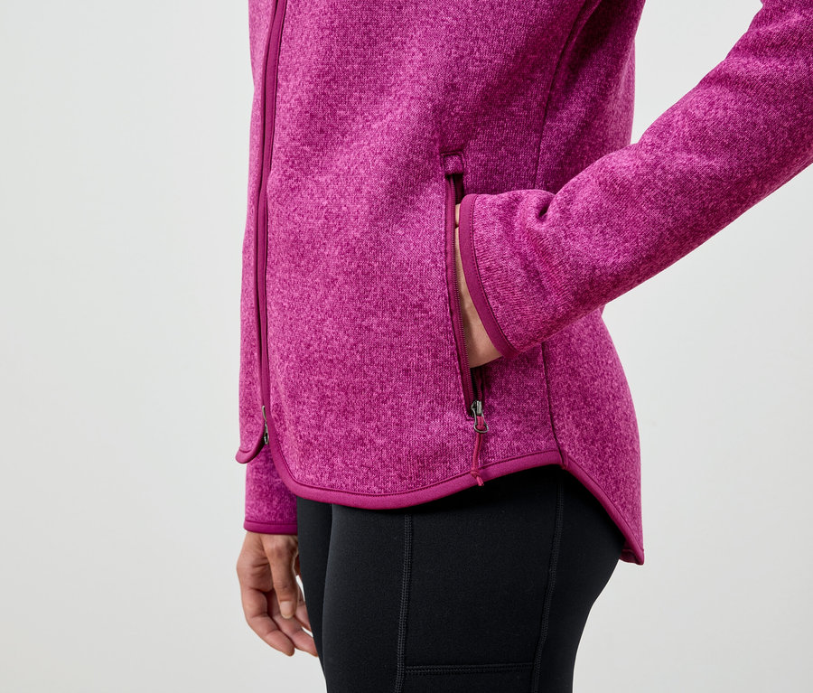 Frau hat ihre Hand in der Tasche einer pinken Fleecejacke und trägt schwarze Leggings.