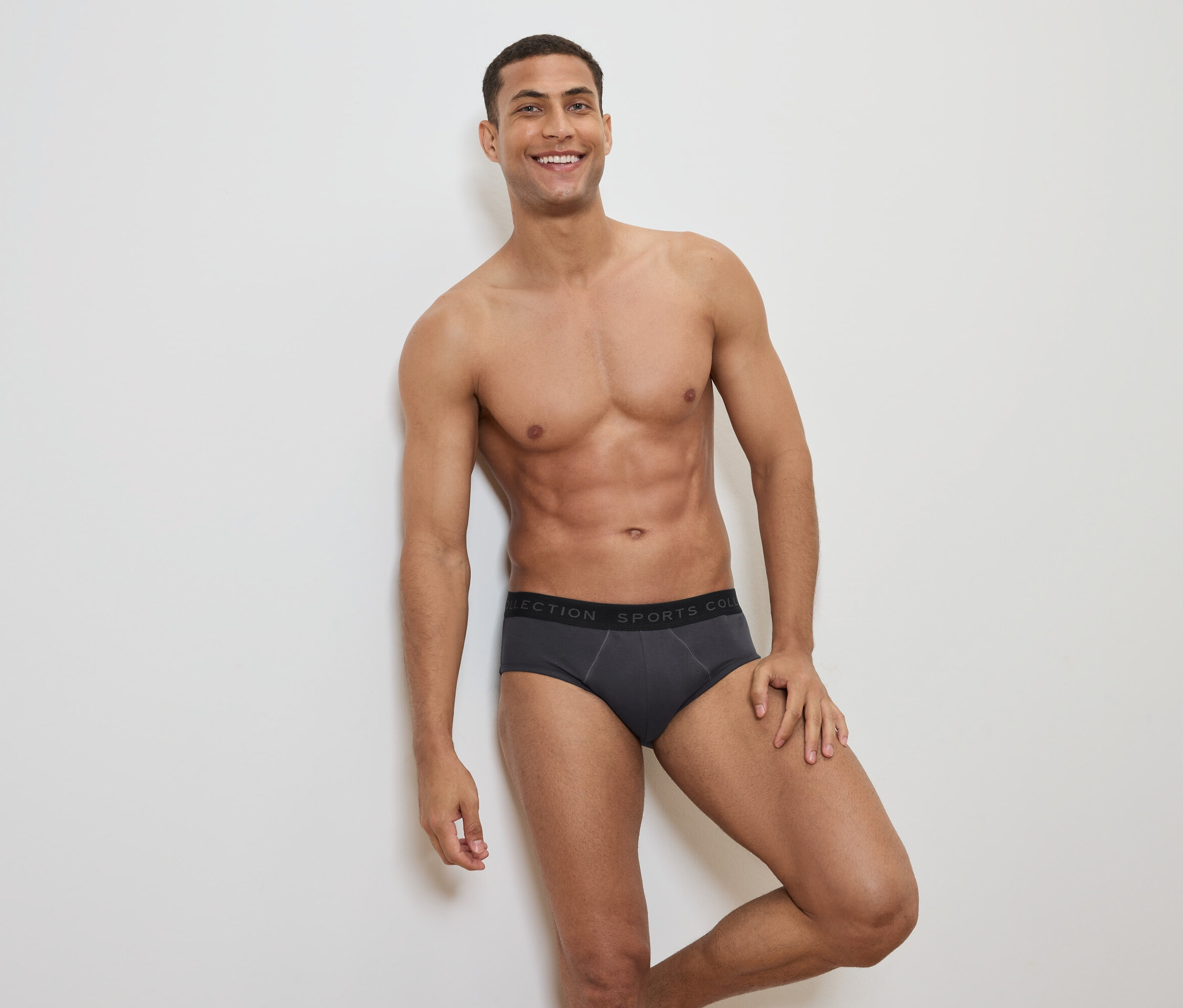 Lächelnder Mann mit freiem Oberkörper posiert in grauer Slip-Unterwäsche mit schwarzem Bund.