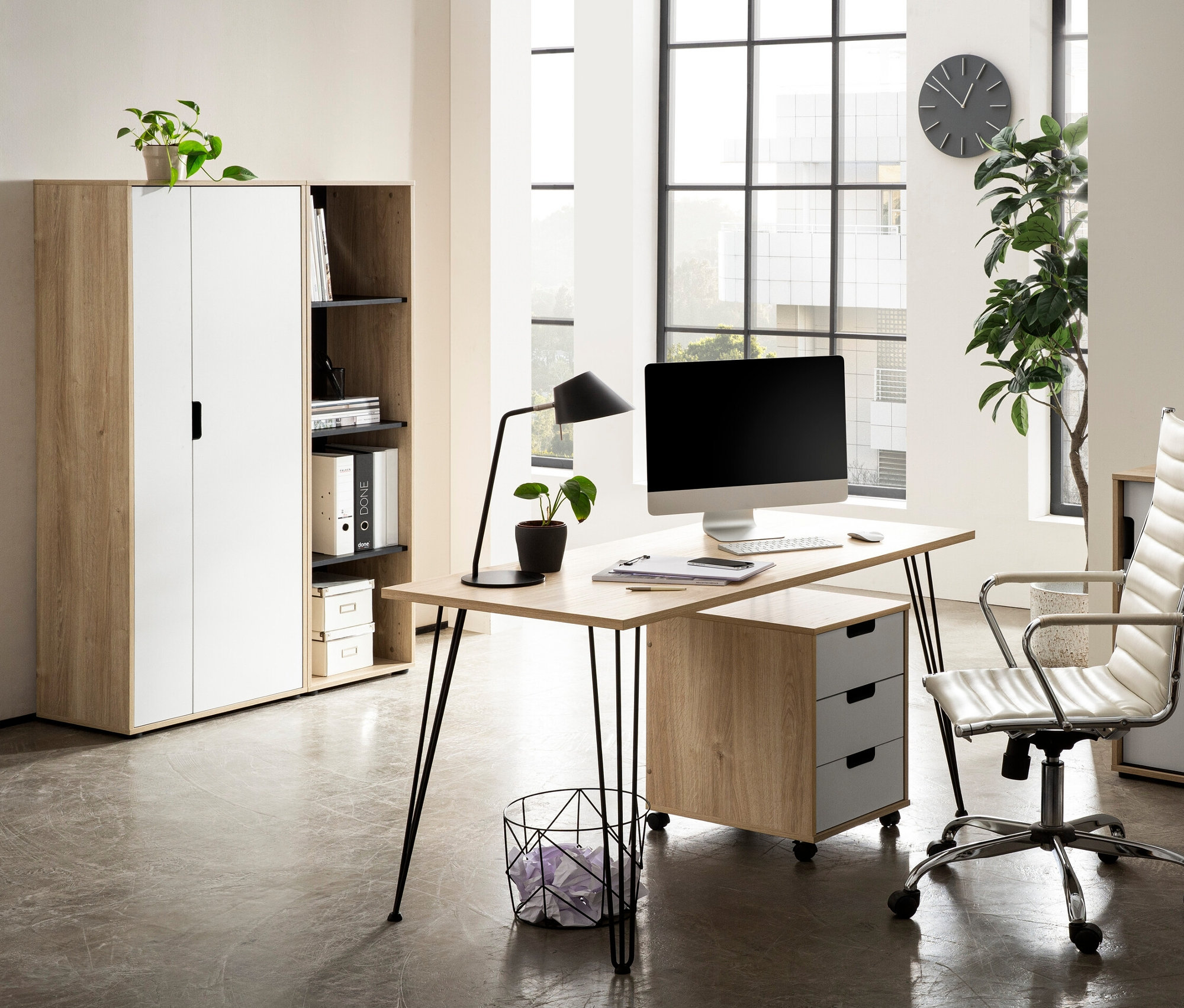 Ein Schreibtisch mit Computer und Lampe steht in einem Raum, daneben steht ein Aktenschrank »Emmik« in Weiß-Eiche.