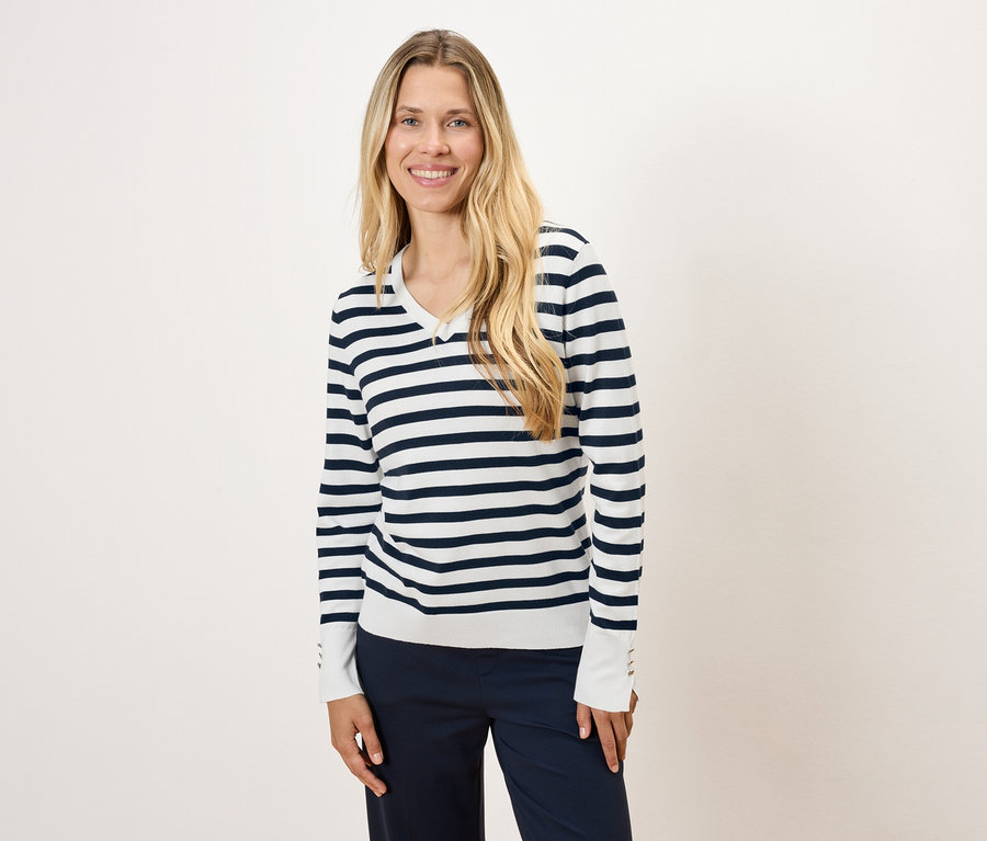 Frau mit langen blonden Haaren trägt einen gestreiften Pullover und eine dunkelblaue Hose.