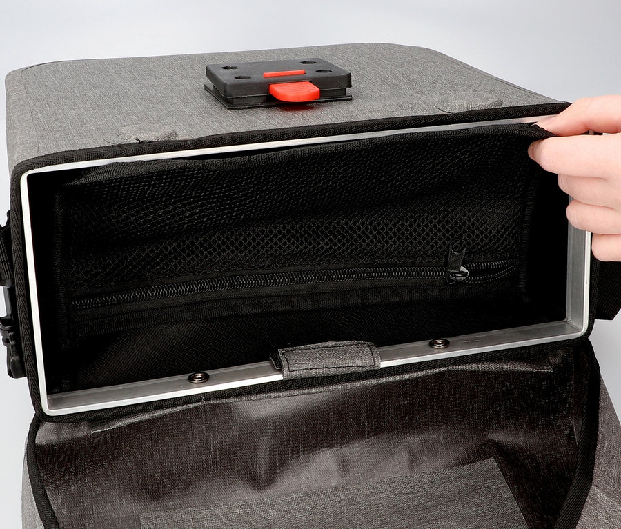 Hand öffnet eine graue Fahrradtasche mit schwarzem Netzfutter und silberfarbenem Rahmen.