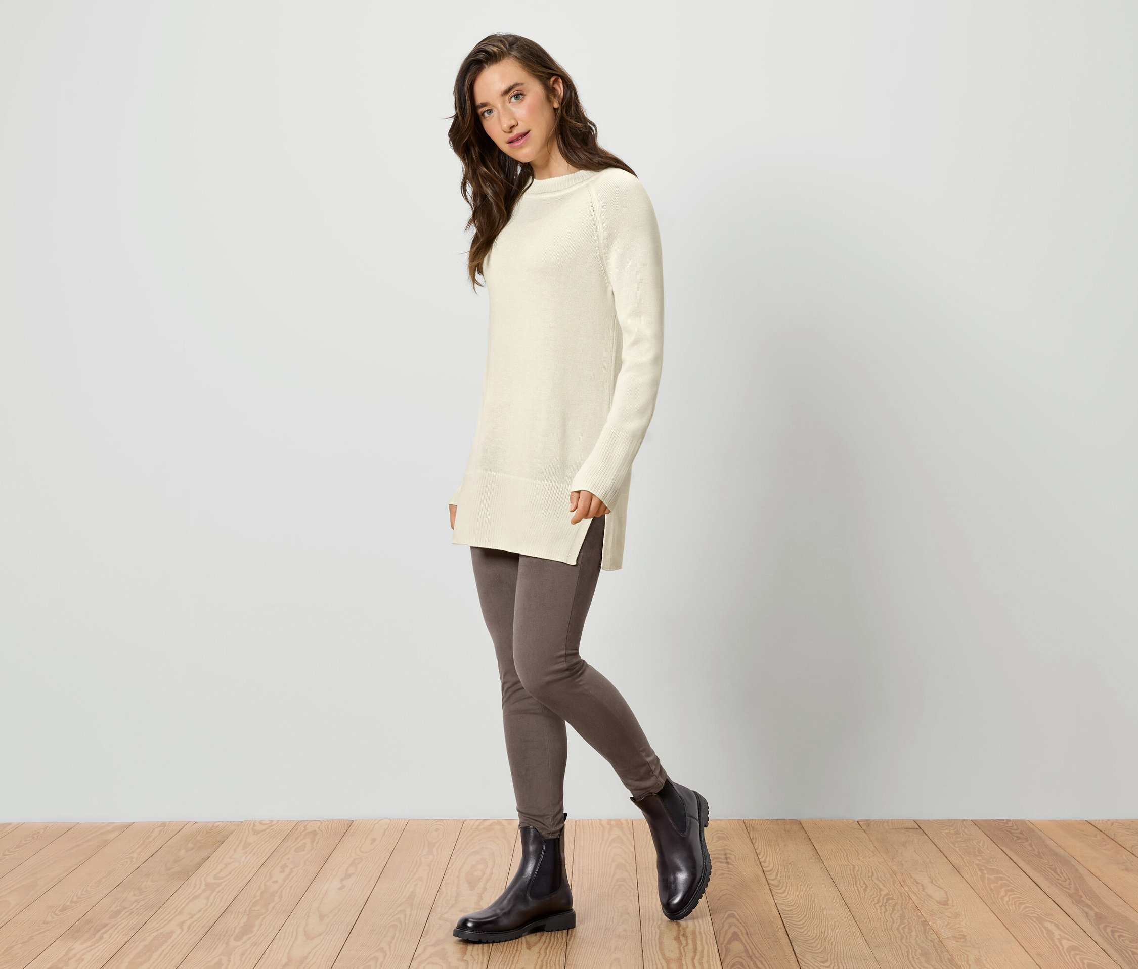 Frau trägt einen langen Strickpullover in Creme, Leggings und Stiefeletten.