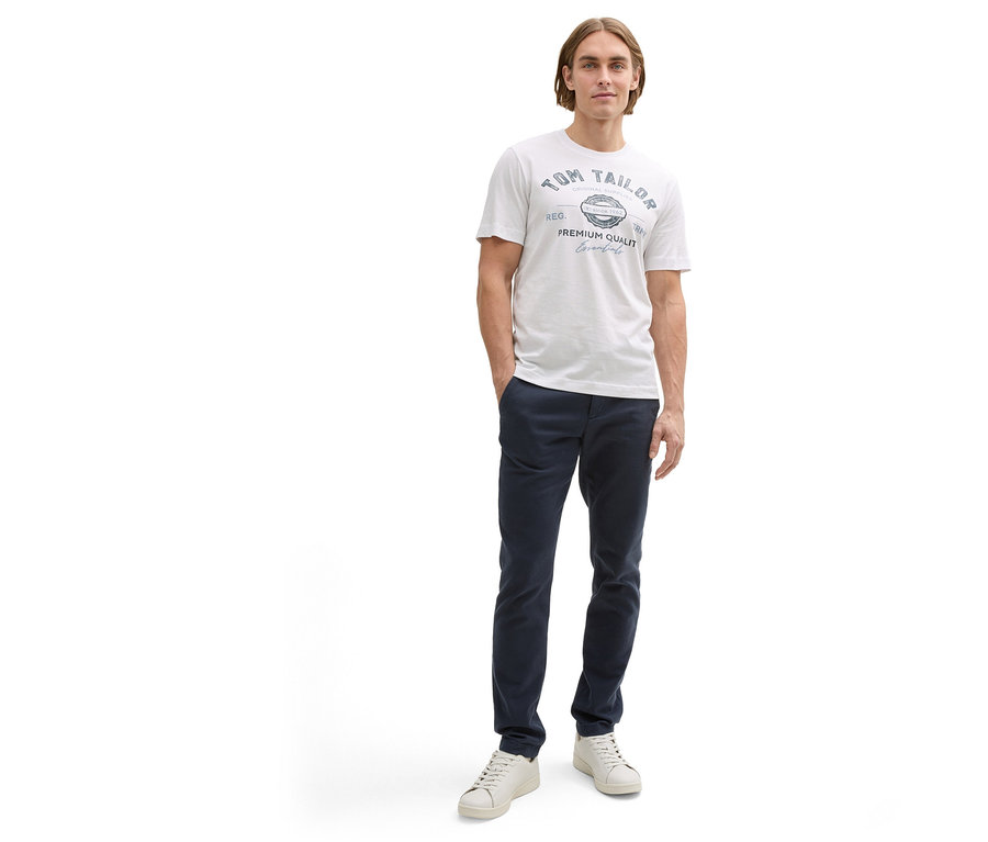 Mann in marineblauer Hose und weißem Tom Tailor T-Shirt mit Logo.