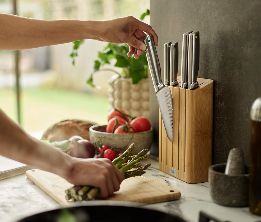 Eine Person nimmt ein Messer aus einem Messerblock auf einer Küchentheke, mit Gemüse im Hintergrund.