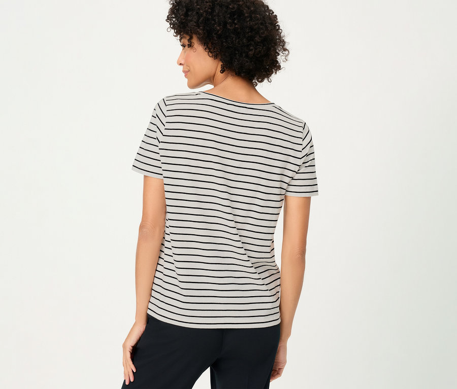 Rückansicht einer Frau mit lockigem Haar im Olsen Shirt mit schwarzen Streifen und schwarzen Hosen.