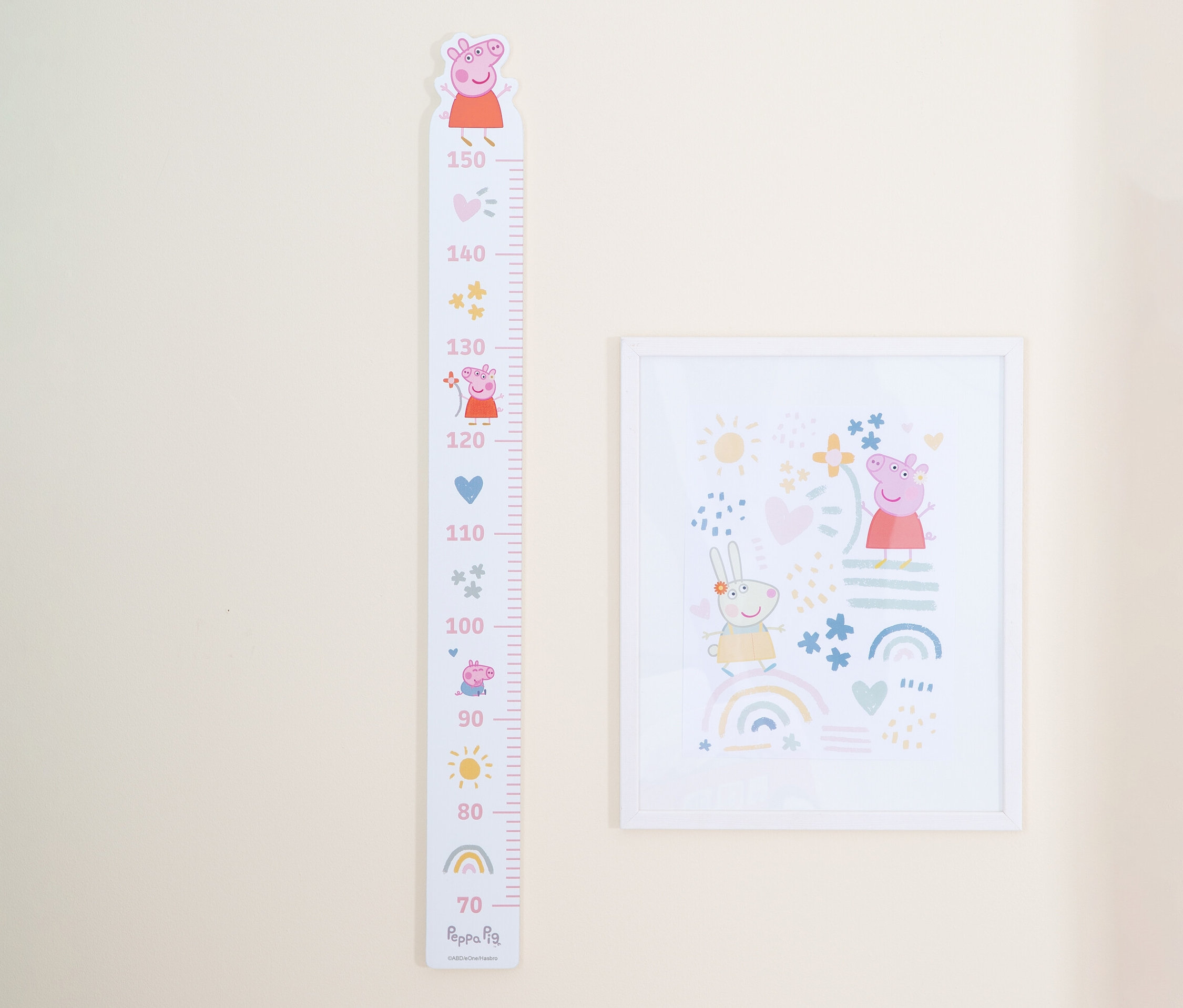 An einer hellbeigen Wand hängen ein Peppa Pig-Wachstumsdiagramm und ein gerahmtes Bild.