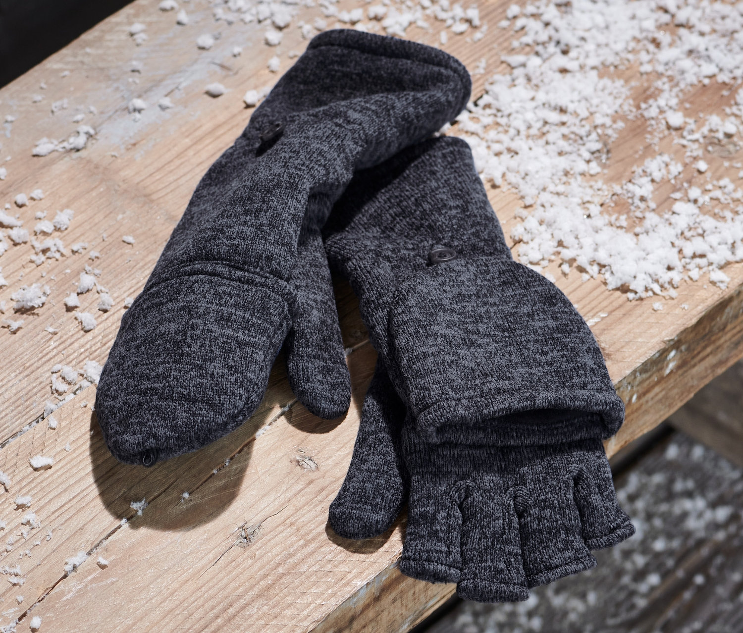 Blaue Strickfleece-Klappfäustlinge liegen neben einem Canvas-Rucksack auf einer Holzbank.