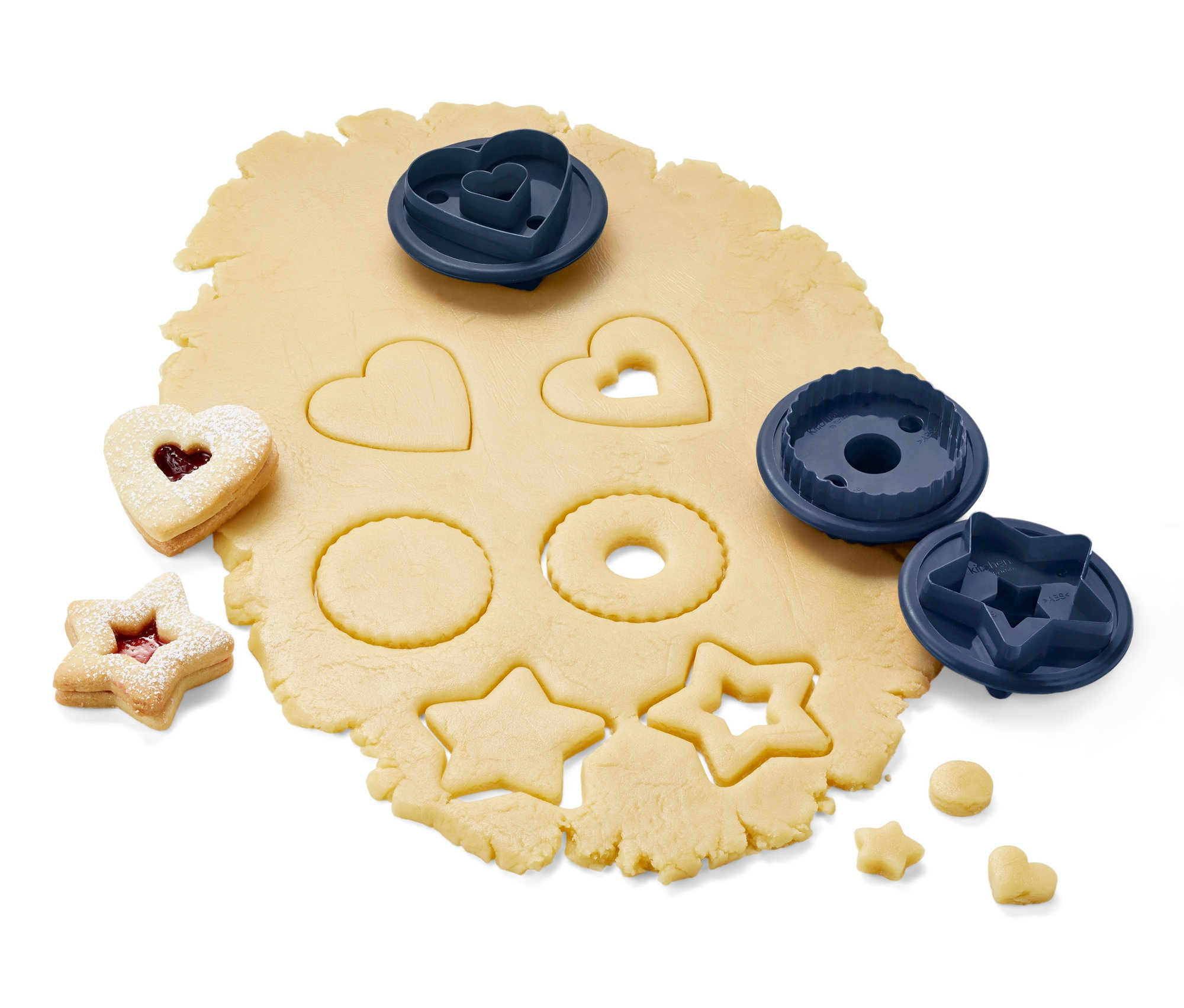 Ausgerollter Teig mit ausgestochenen Formen und 3 Linzer-Plätzchen-Ausstecher.