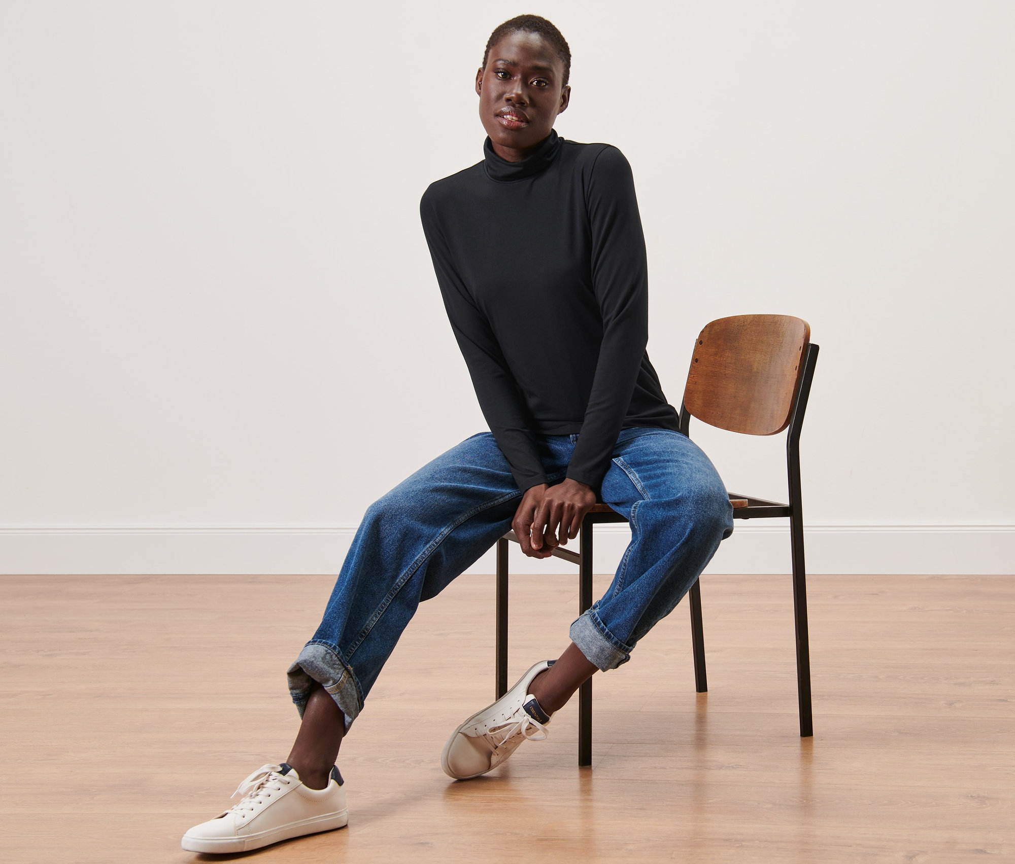 Frau sitzt auf einem Stuhl und trägt ein schwarzes Rollkragenshirt.