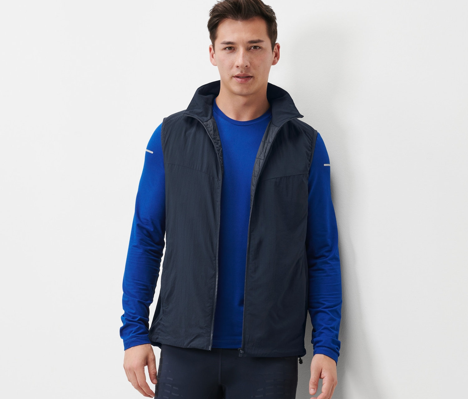 Mann trägt eine Funktionsweste, ein blaues Langarmshirt und dunkle Leggings.